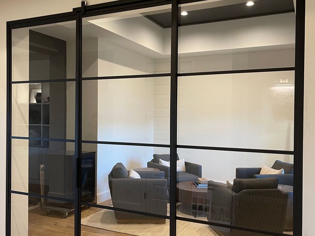 Black-framed glass wall with sliding barn door opening onto a sitting room