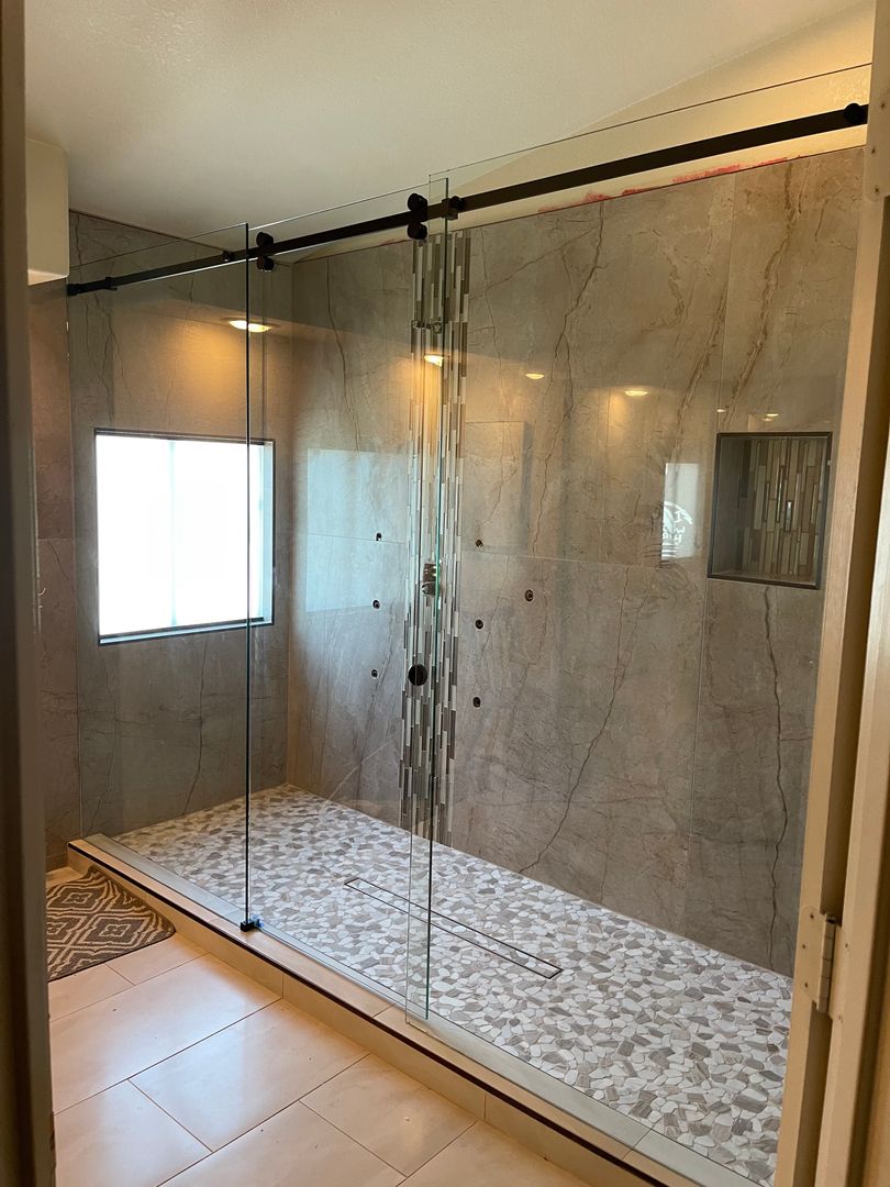 Frameless glass shower enclosure with a barn door slider, grey marble tile and a pebble floor