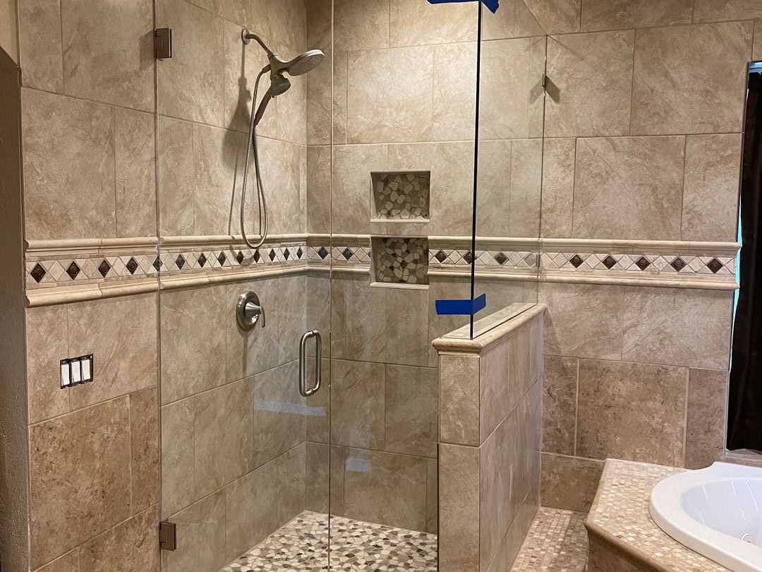 Frameless glass shower enclosure with beige travertine tile and a diamond mosaic border