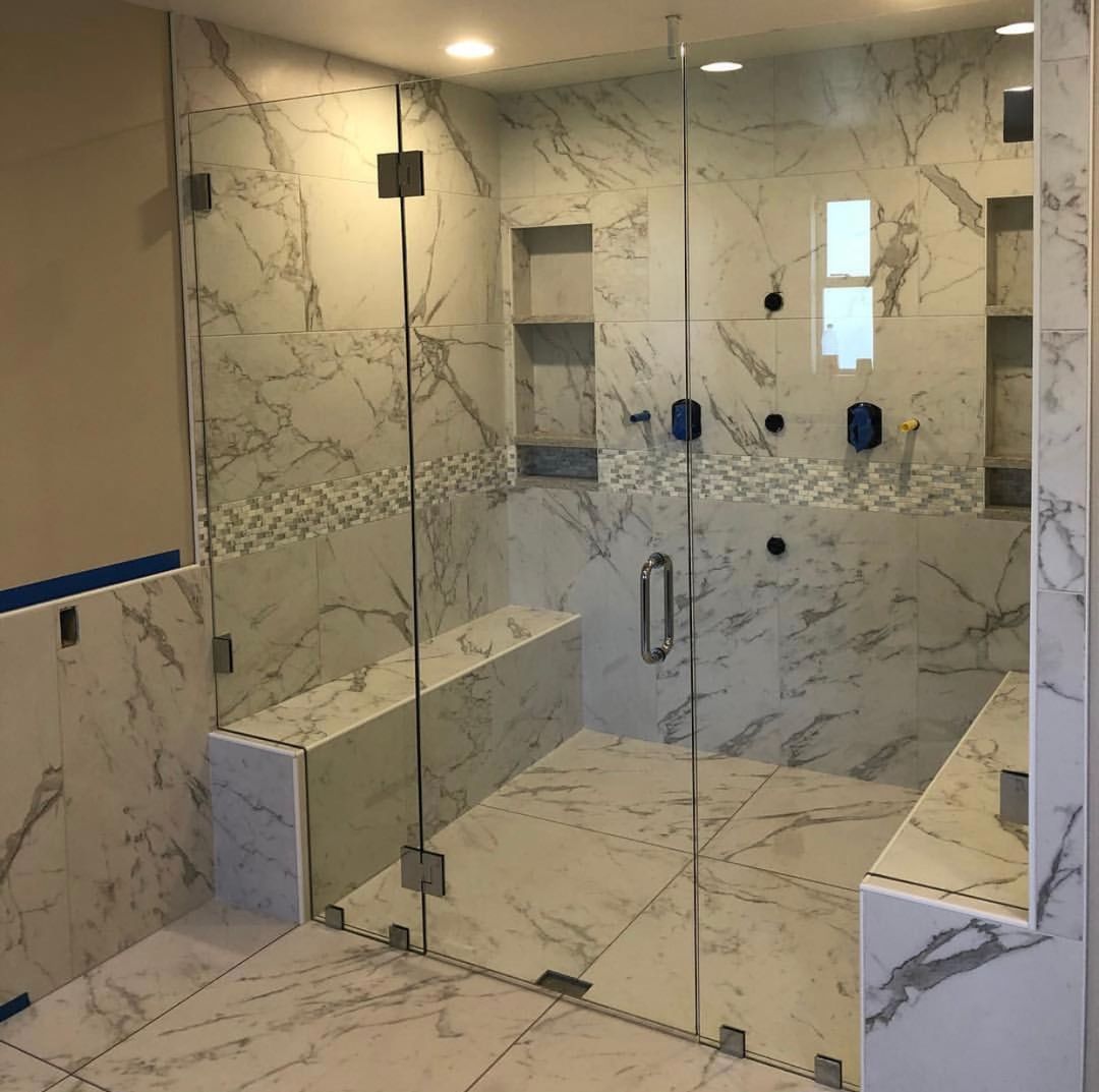 Frameless glass shower enclosure with marble mosaic tile and a built-in bench seat