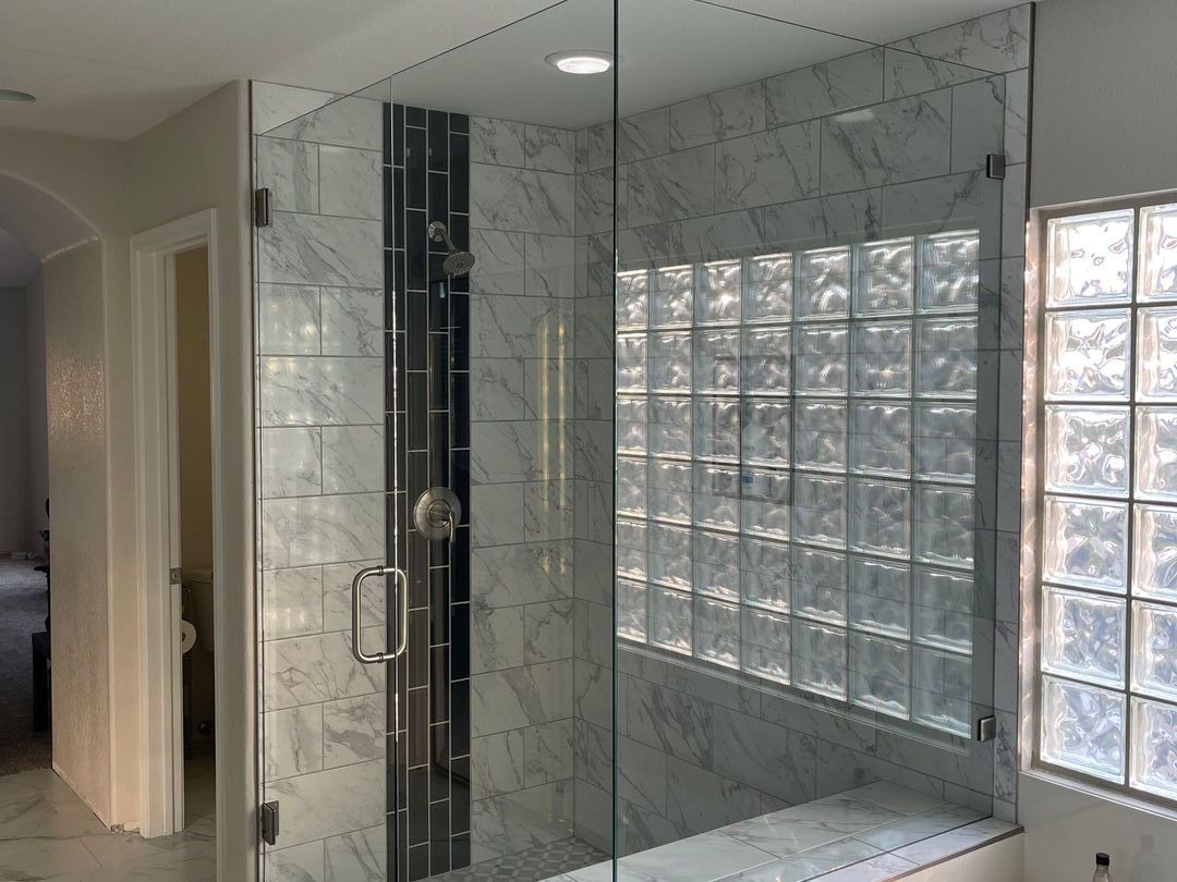 Frameless glass shower with marble tile, a dark vertical accent stripe and a glass block window
