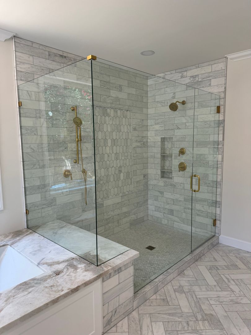 Frameless glass shower enclosure with marble subway tile and satin brass hardware