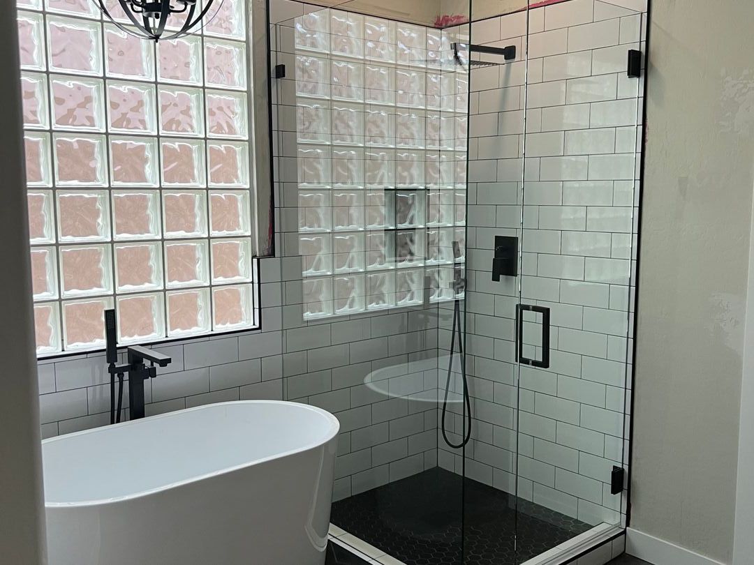 Frameless glass shower with white subway tile, a glass block window and matte black hardware beside a freestanding tub