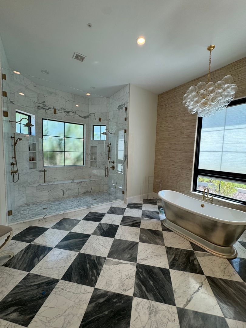Frameless glass shower enclosure in a Scottsdale marble bathroom with checkerboard marble floor and a freestanding metal tub